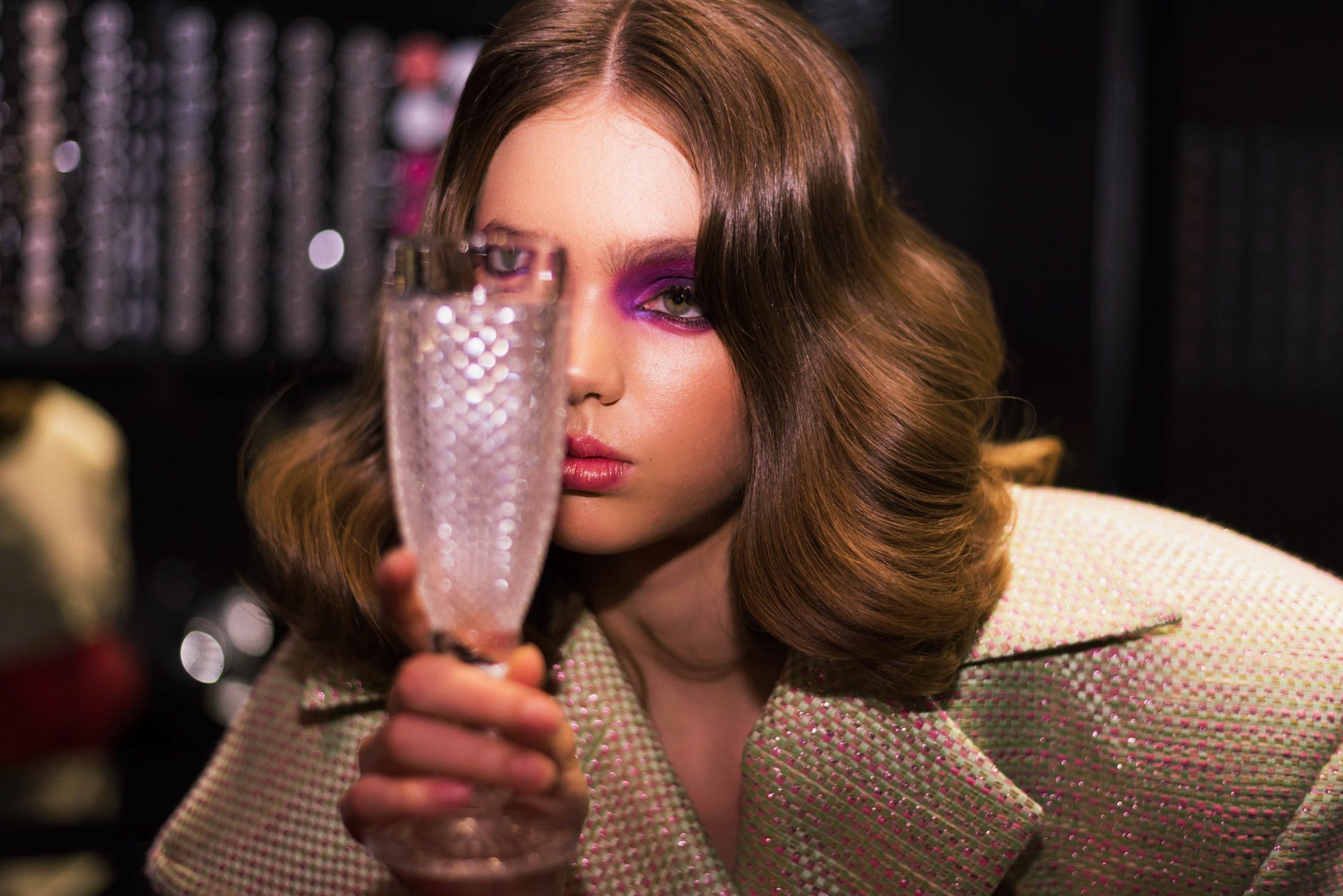 woman wearing trendy coat and makeup with glass in bar